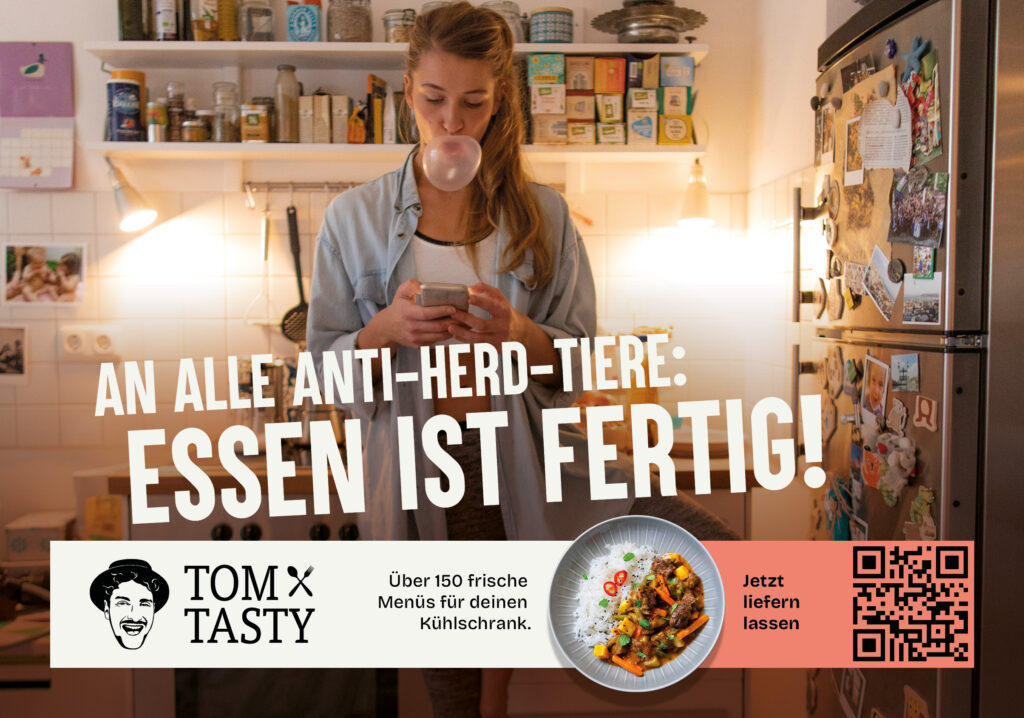 Anzeigensujet mit Frau die ihr Smartphone in der Hand hält, mit dem Slogan: "AN ALLE ANTI-HERD-TIERE:
ESSEN IST FERTIG!"
